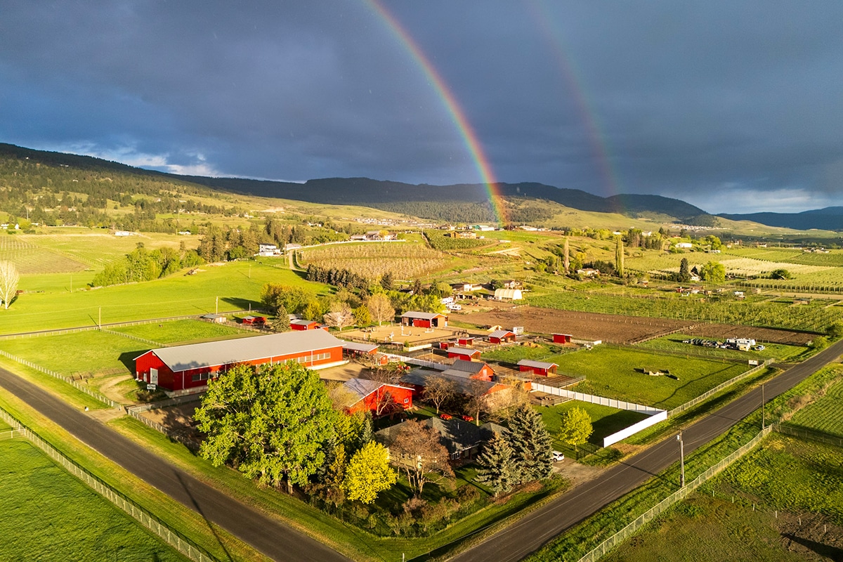 Aerial view of a rural farm with red barns, green fields, and a rainbow in the sky.